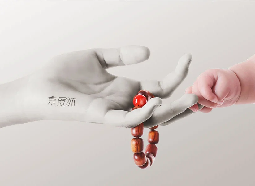 傳家之寶手鍊-照片中，一隻象徵長輩或祖輩的灰階大手，與一隻稚嫩紅潤的嬰兒小手輕輕接觸。這種鮮明的膚色與質地對比，象徵著生命的延續與時間的更迭!
